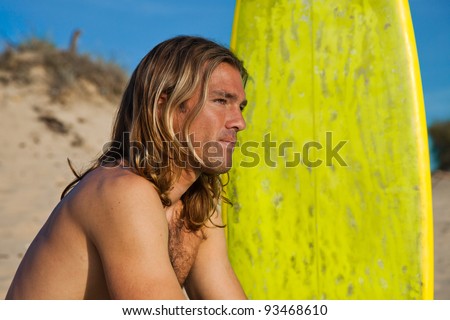Cute long haired blonde surfer sitting next to his surfboard.
