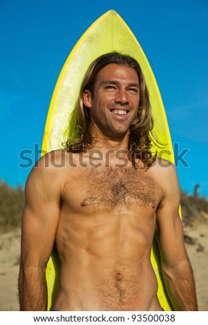 Sensual long haired blonde surfer smiling in front of his surfboard.