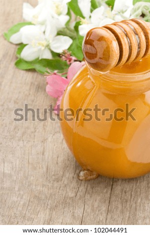 honey in glass and stick with blossom on wood background