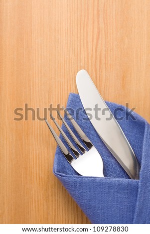 silver fork and knife as utensils in napkin on wooden background