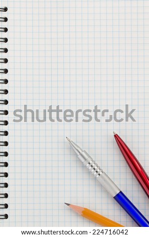 pen and pencil at checked paper of notebook