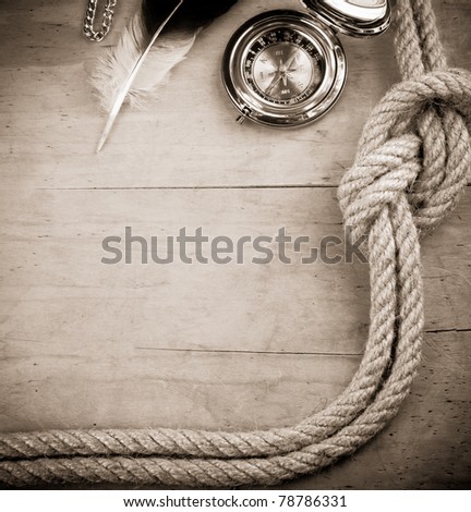 ship ropes and compass with feather on wood background board