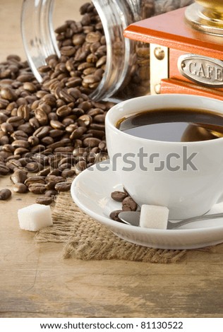 cup of coffee and grinder with roasted beans on wooden
