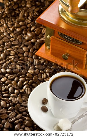 cup of coffee and grinder with roasted beans on straw