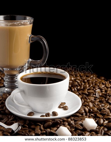 cup of coffee and glass on roasted beans as background isolated on black background