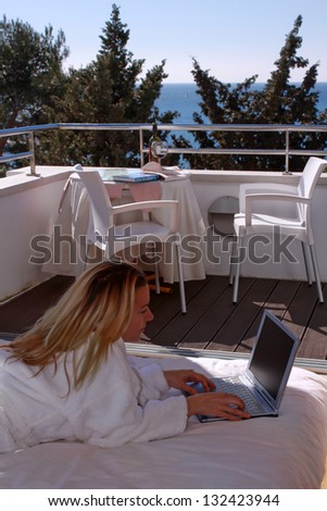 Relaxed woman in bathrobe clothes laying on bed with notebook and sea view