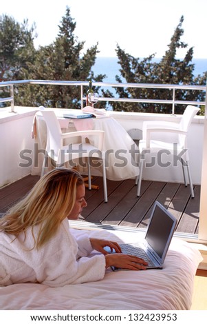 Relaxed woman in bathrobe clothes laying on bed with laptop and sea view