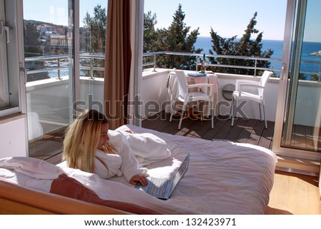 Girl in hotel room laying on bed with notebook and ocean view