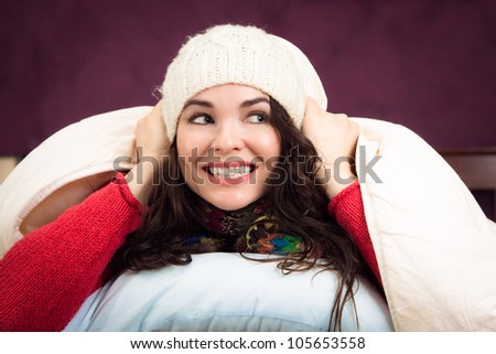 A beautiful happy young woman peeking out from underneath the blankets of her bed