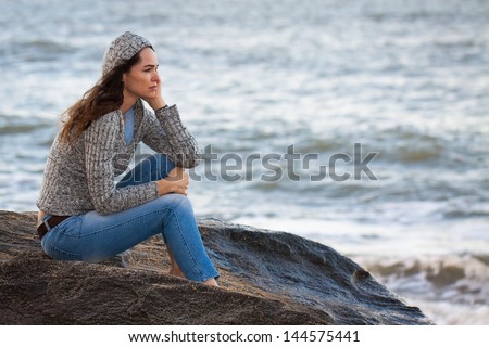 Sad and thoughtful woman sitting by the water deep in thought.