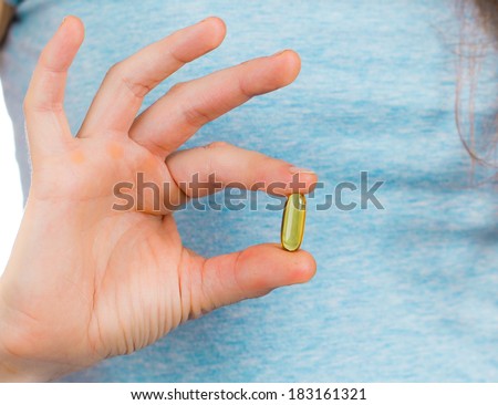 A woman\'s fingers holding a omega 3 or fish oil capsule.