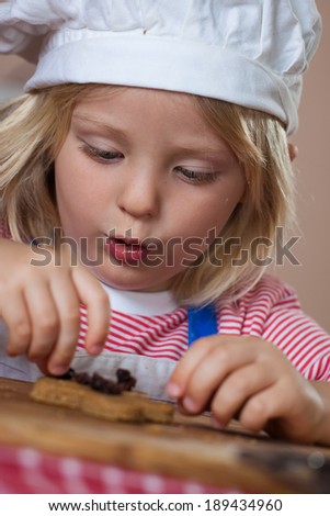 A cute young happy boy is baking and putting raisins on a gingerbread man.
