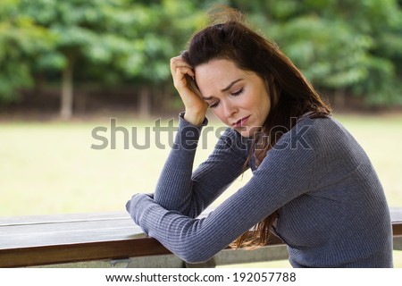 A sad and upset woman sitting down alone outdoors