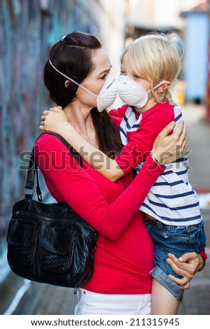 A concerned woman carrying her son. Both are wearing protective face masks for pollution or virus.