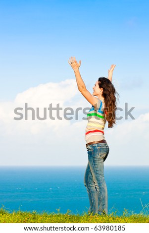 A young attractive woman with her hands in the air and smiling in front of a beautiful ocean