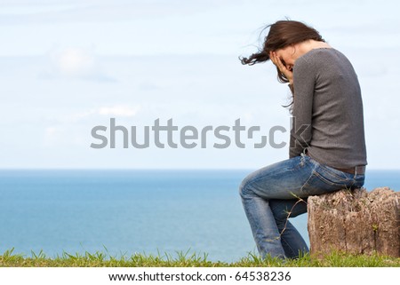 A strong image of a depressed and upset young woman sitting outside with her head in her hands