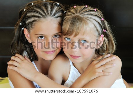 Two little girls with blond and brunette twists hairstyle embraced in a hug