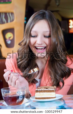 Young happy girl sitting in cafe and having cake for desert and laughing gleefully