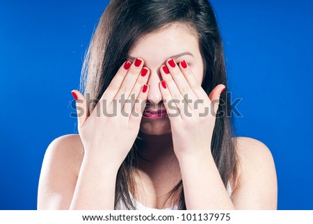 Young teenage girl closing eyes with hands over blue screen background