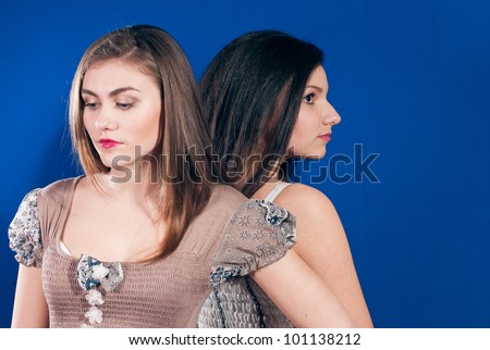 Two young beautiful girls standing back to back on blue screen background