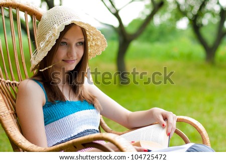 Portrait of a Beautiful young woman relaxing by sitting and reading book in rocking chair in the spring or summer outdoors with green grass and some trees of garden or park on the background