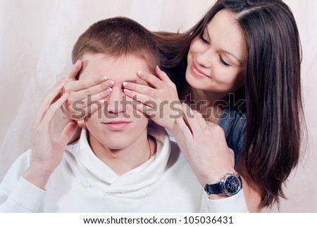 Portrait of a beautiful happy smiling woman covering eyes with her hands of handsome young man in fun mood