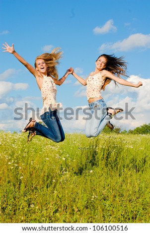 Happy jump: two beautiful happy smiling young women jumping on a bright day of summer on the blue sky and green grass background