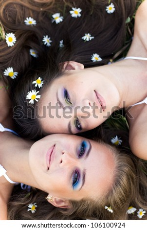 Two beautiful brunette and blond women  lying head to head with camomile flowers in hair