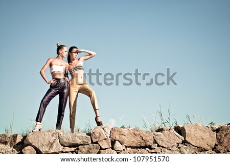 Two fashion girls standing against blue sky and looking far away