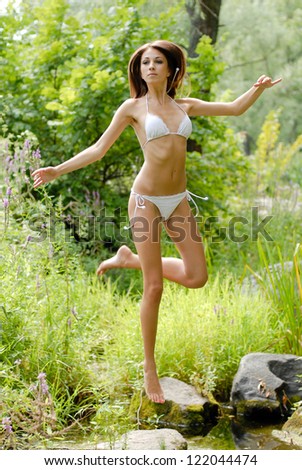 Young beautiful woman in white swimsuite in savage forest jumping