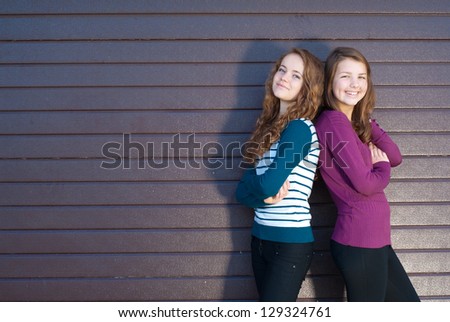 Two best teenage girlfriends standing back to back against grey violet background