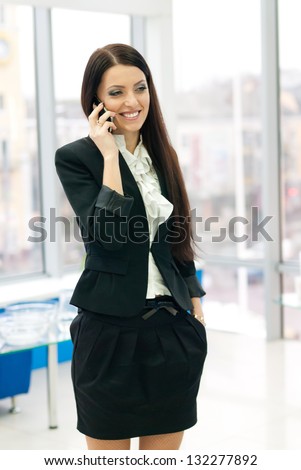 Young successful business female woman in formal suit speaking on mobile phone by office window