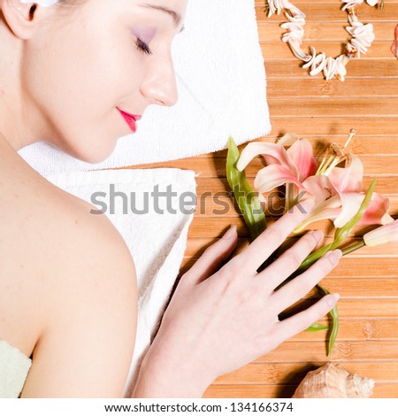young beautiful woman laying on bamboo mat with hand on flower relaxing in spa salon eyes closed