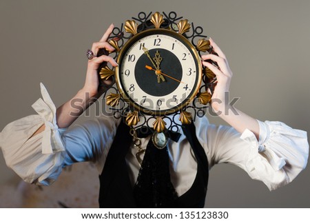 Five to Twelve Face clock. A girl holding a clock in the head, on a gray wall background