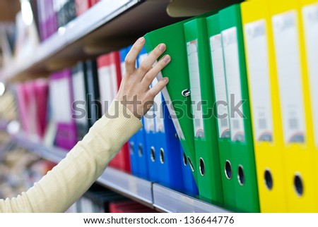 woman\'s hand holding big folder from the shelves with office files.