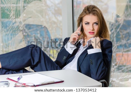 Business woman in man\'s suit & shirt relaxing & talking on phone in the office