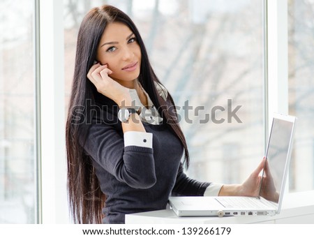 Portrait of a happy young business woman using notebook PC relaxing near office window indoors
