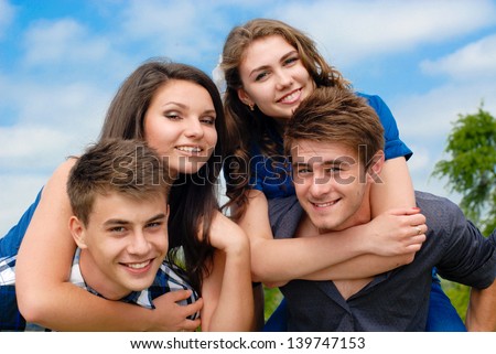 Four happy teenage friends boys and girls outdoors against blue sky background