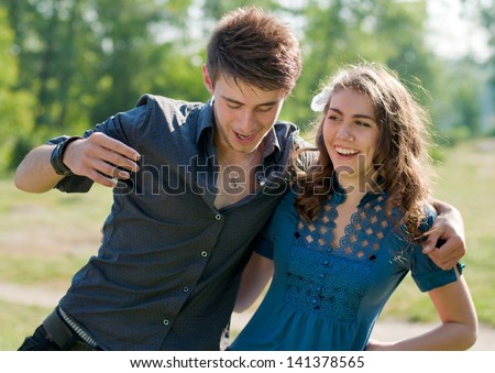 Happy funny teenage couple dancing outdoors and laughing on the bright sunny day & green summer background