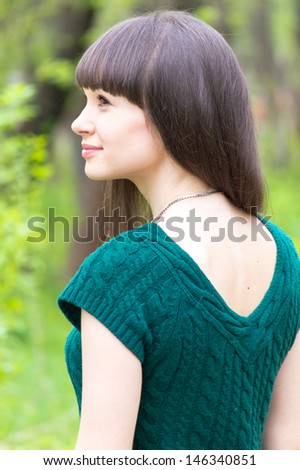 Beautiful young woman in park wearing knitted green blouse rear view