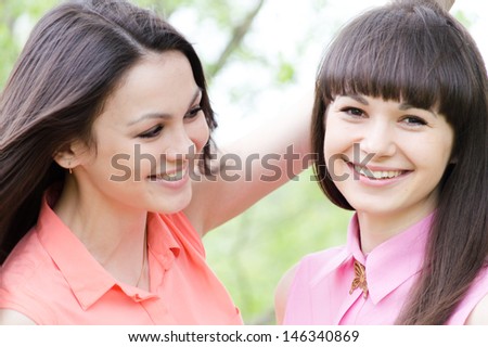 Two sisters or girl friends smiling, laughing and hug outdoors in spring or summer