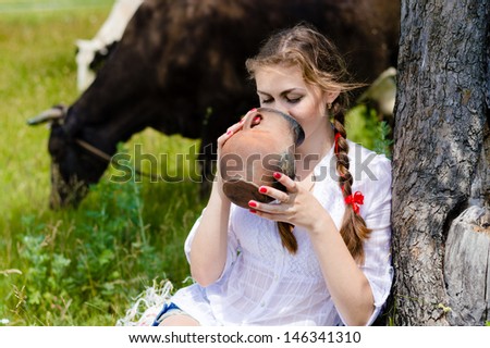 Young happy woman drinking fresh milk near cows in countryside on summer day