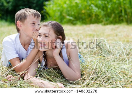 Teenage happy smiling sister and little brother sitting on hay outdoors on the summer day green background