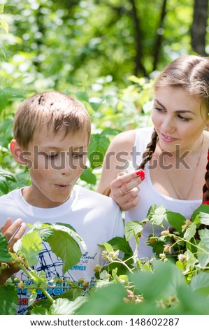 Teenage sister and little brother happy eating raspberry outdoors on the summer day green outdoors background