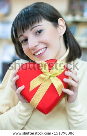 Happy young smiling beautiful woman holding red gift box in form of heart