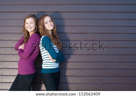 Two best teen girlfriends standing back to back against gray violet background