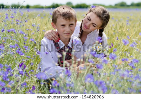Teenage sister and little brother hugging outdoors happy smiling & looking at camera on summer day background