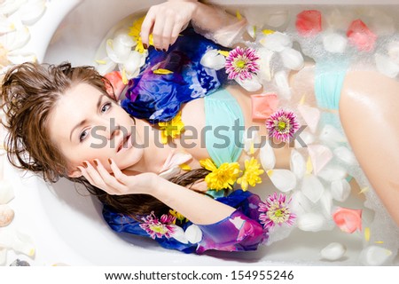 Beautiful sensual lady looking at camera taking a bath with flower petals