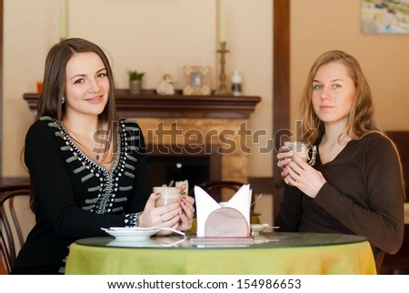 very cute happy women drinking coffee sitting inside in cafe bistro happy smiling & looking at camera
