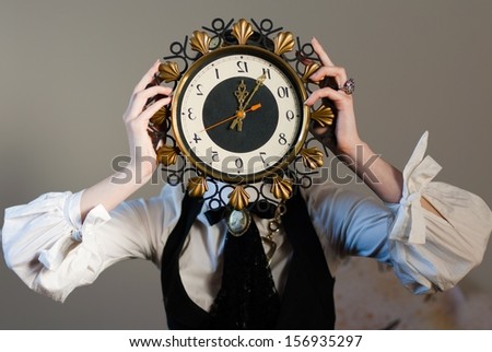 Five to Twelve: girl holding a clock in the head, on a gray wall background